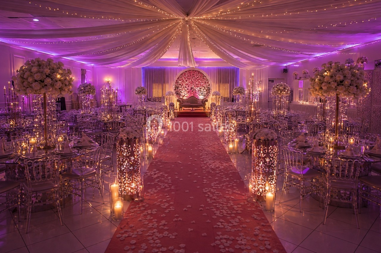 Salle de réception décorée avec des guirlandes lumineuses, des fleurs blanches et une allée centrale rouge parsemée de…