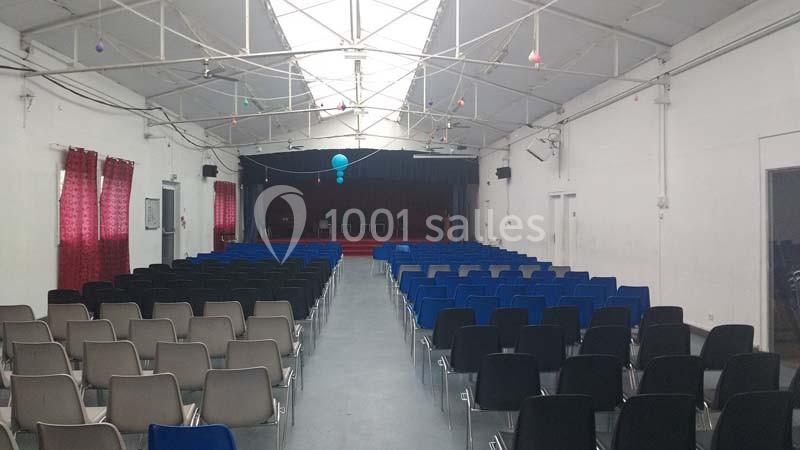 Salle de conférence vide avec des rangées de chaises colorées face à une scène équipée d'un rideau rouge.