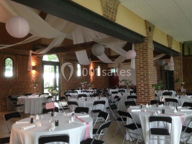 Salle de réception avec murs en briques, tables rondes dressées et décorations suspendues en tissu et lanternes.