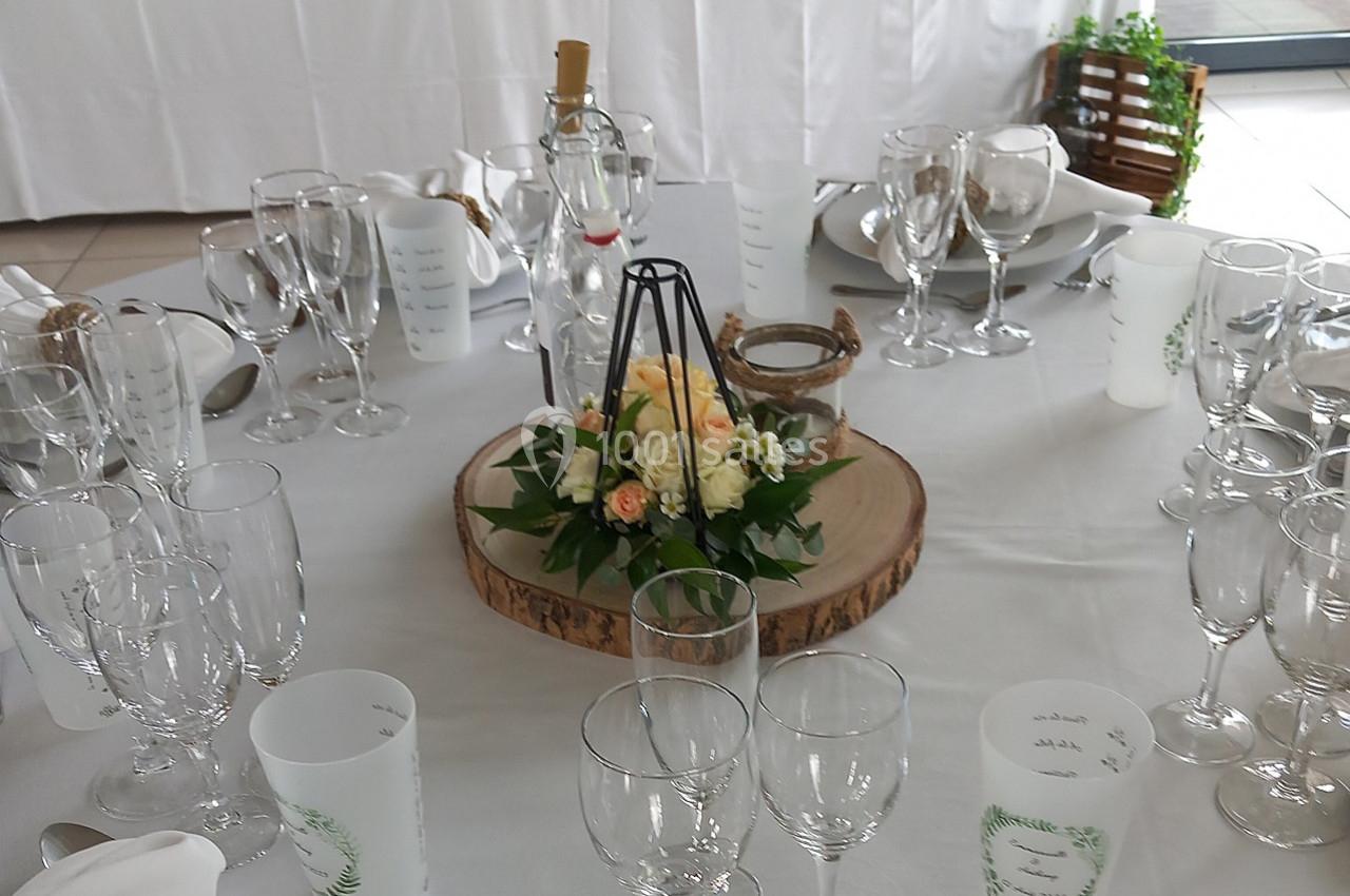 Table dressée avec des verres, des gobelets personnalisés, un centre de table floral sur rondin de bois et des décorations.