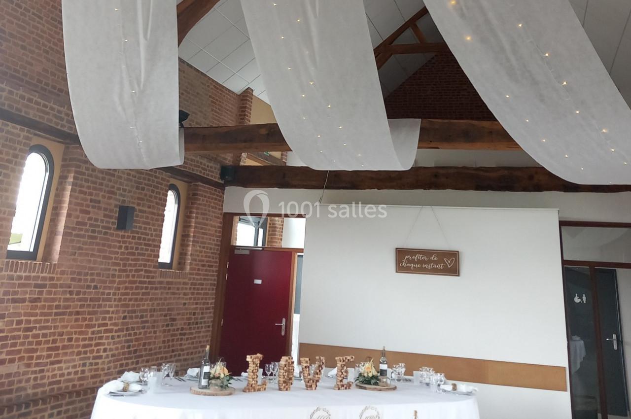 Salle de réception décorée avec des voilages suspendus, une table dressée et un mur en briques apparentes.