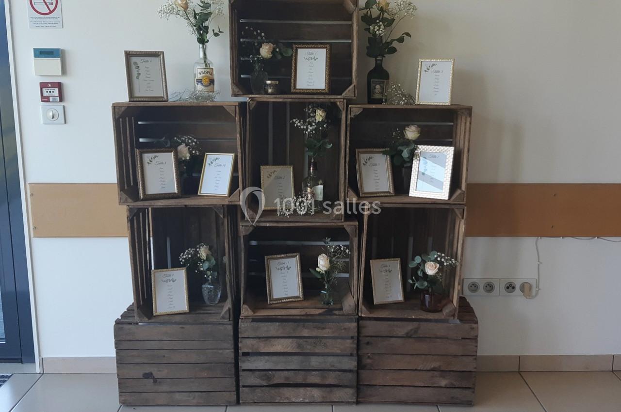 Empilement de caisses en bois décorées de fleurs, cadres et bougies, disposées dans un espace intérieur.