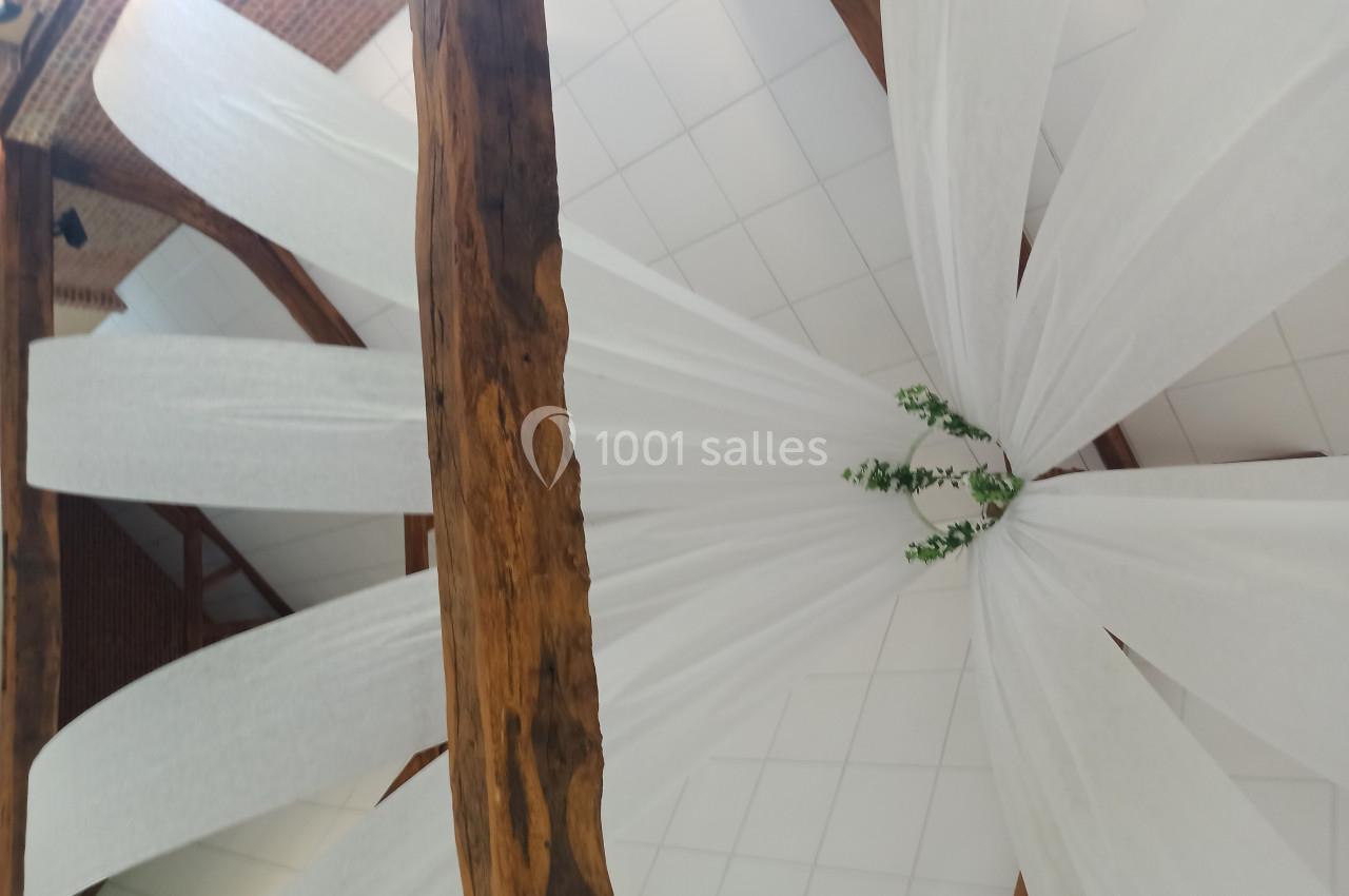 Plafond décoré de voilages blancs suspendus à des poutres en bois, avec des branches vertes au centre.