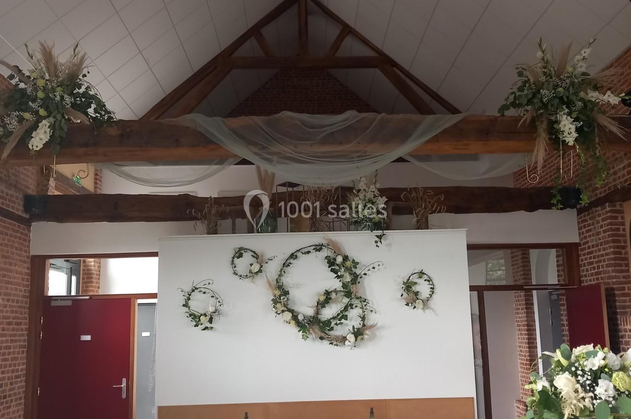 Salle de réception décorée pour un mariage, avec des tables dressées, des chaises ornées de rubans verts et des fleurs…