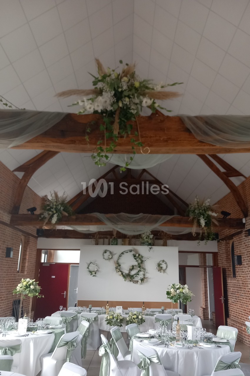 Salle de réception décorée avec des fleurs blanches, des voilages suspendus et des tables dressées élégamment.