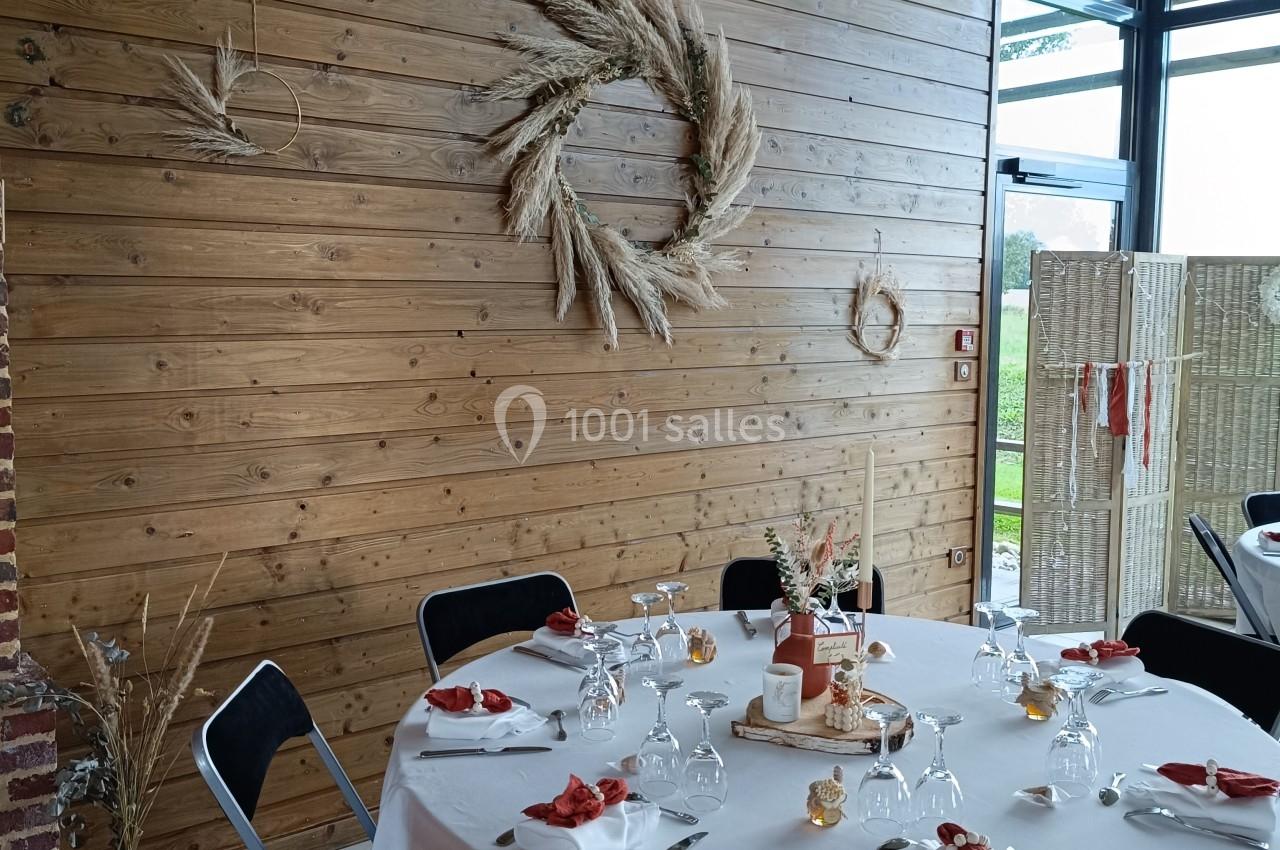 Table ronde dressée pour un repas, décorée de serviettes rouges, avec un mur en bois orné de couronnes de fleurs séchées.