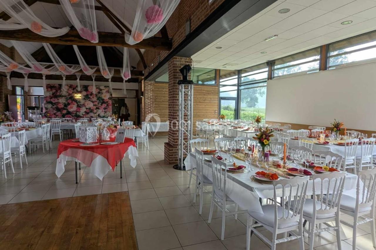 Salle de réception décorée pour un événement, avec tables dressées, nappes blanches et ornements floraux.