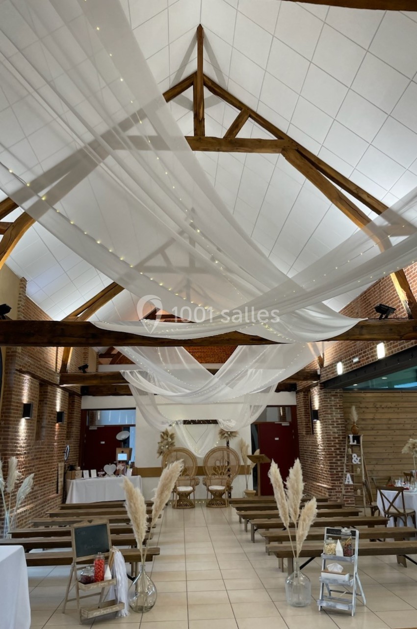 Salle décorée pour une cérémonie avec voilages suspendus, bancs en bois et ornements floraux dans une ambiance champêtre.