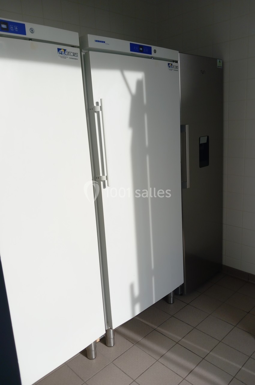 Deux grands réfrigérateurs blancs et une armoire métallique dans une pièce carrelée.