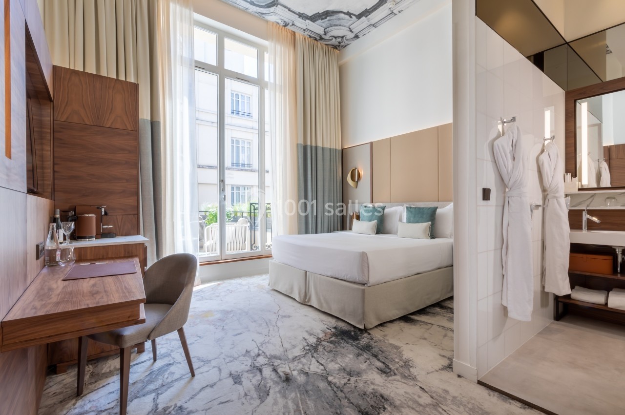 Chambre lumineuse avec un lit double, un bureau en bois, des peignoirs accrochés et une grande fenêtre donnant sur l…