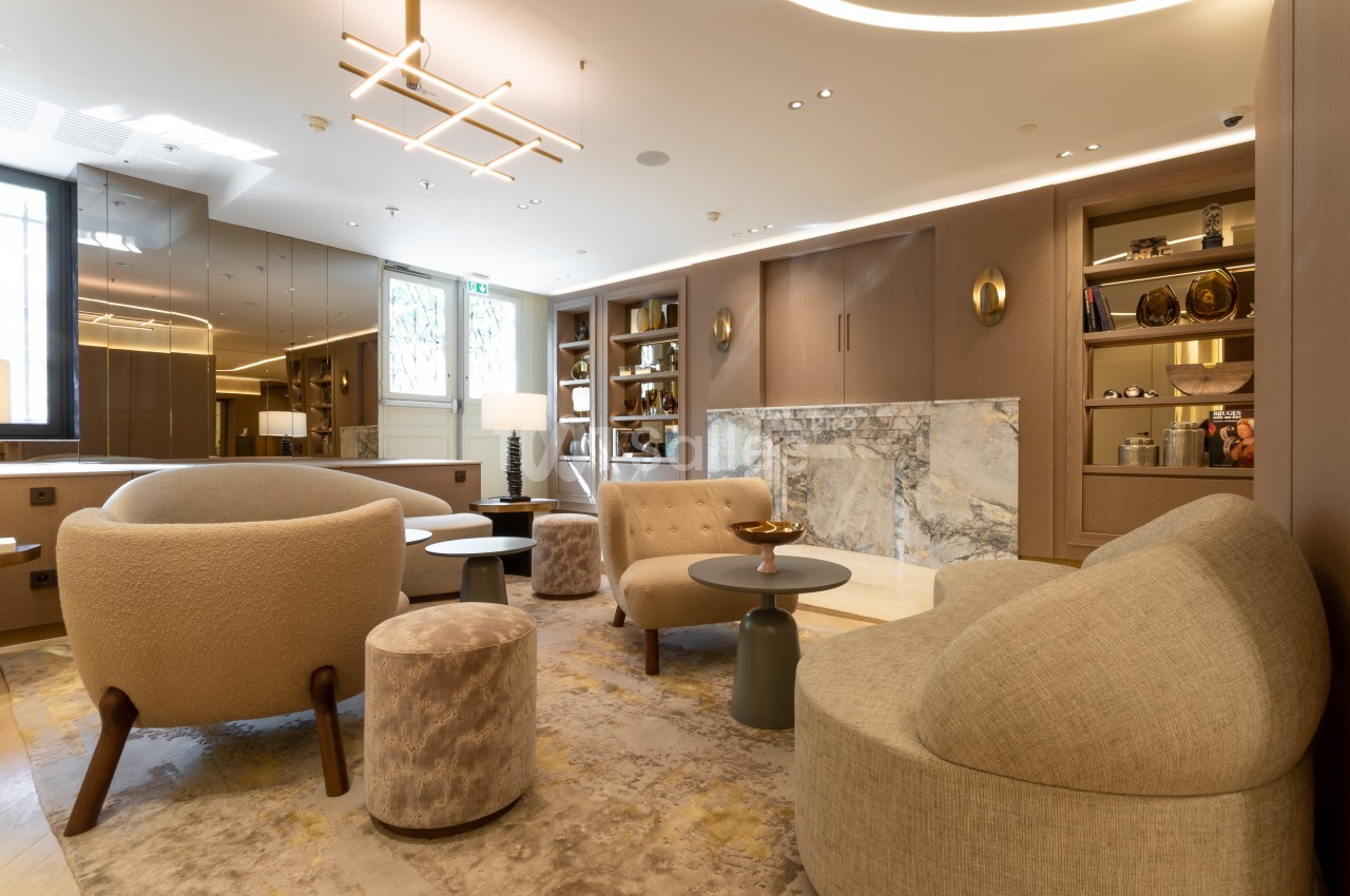 Salon moderne avec fauteuils, tables basses, cheminée en marbre et étagères intégrées, éclairage doux.