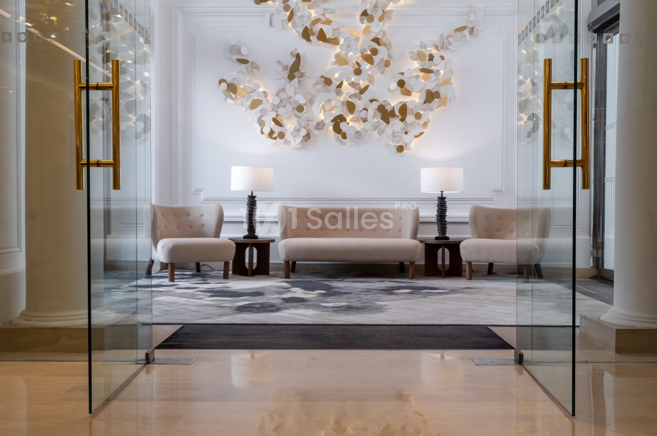Salon élégant avec canapé beige, deux fauteuils assortis, tables en bois sombre et décoration murale artistique.