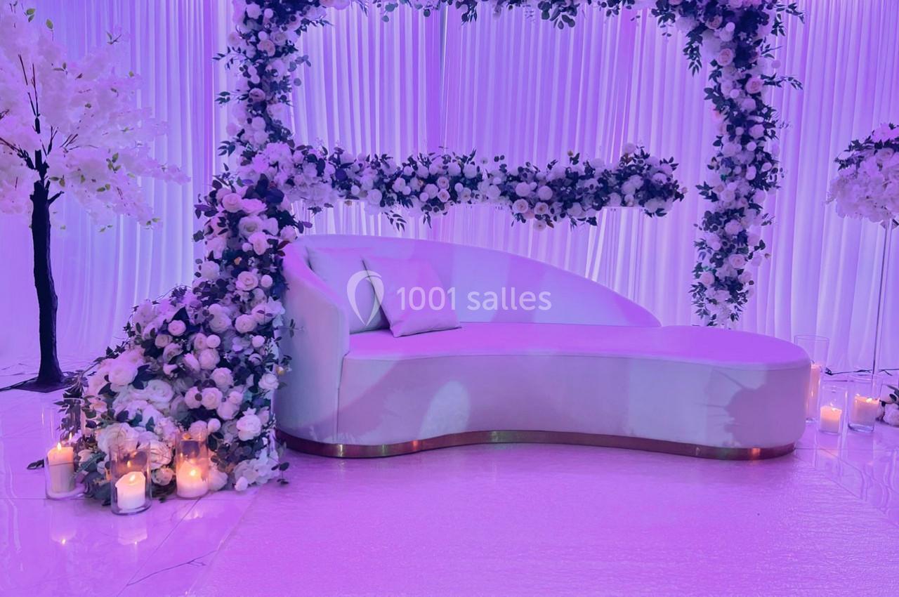 Location salle Brétigny-sur-Orge (Essonne) - La Joya Réception #2 Canapé blanc entouré de fleurs blanches et violettes, avec des bougies allumées sur un sol brillant.