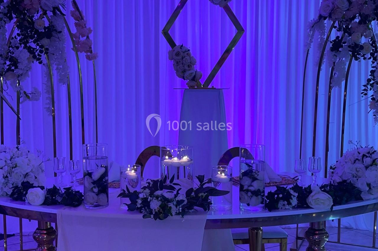Location salle Brétigny-sur-Orge (Essonne) - La Joya Réception #15 Table décorée pour un événement avec fleurs blanches, bougies allumées et arrière-plan violet illuminé.