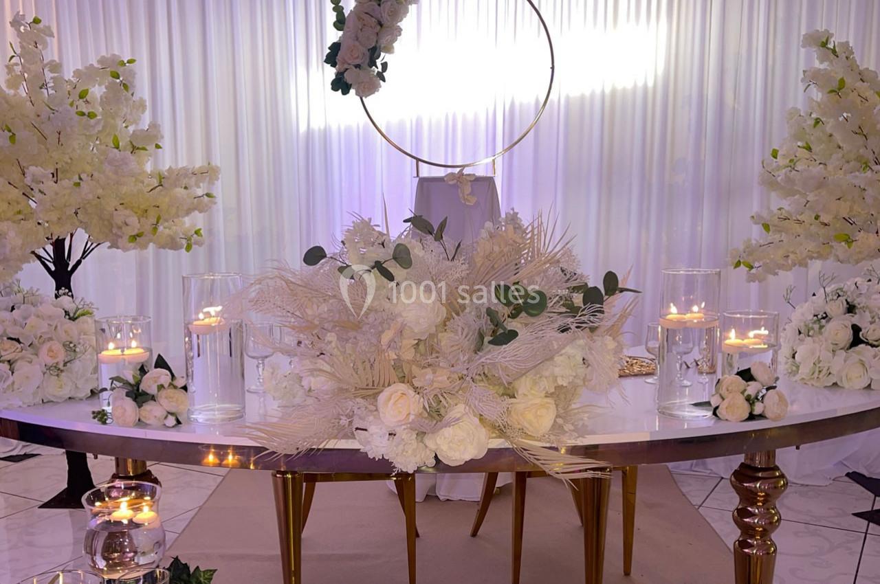 Location salle Brétigny-sur-Orge (Essonne) - La Joya Réception #10 Décoration de table élégante avec fleurs blanches, bougies allumées et arche circulaire ornée de fleurs en arrière-plan.
