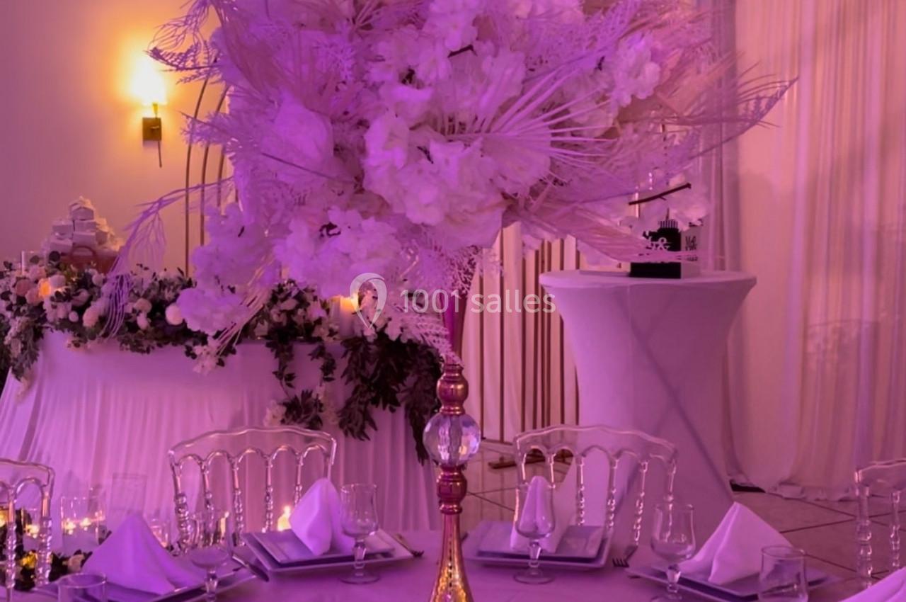 Location salle Brétigny-sur-Orge (Essonne) - La Joya Réception #20 Centre de table floral avec des fleurs blanches et roses sur une table dressée dans une salle de réception éclairée.