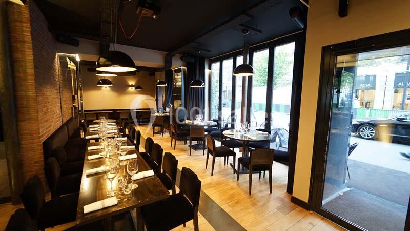 Salle de restaurant moderne avec tables dressées, grandes baies vitrées et éclairage suspendu.