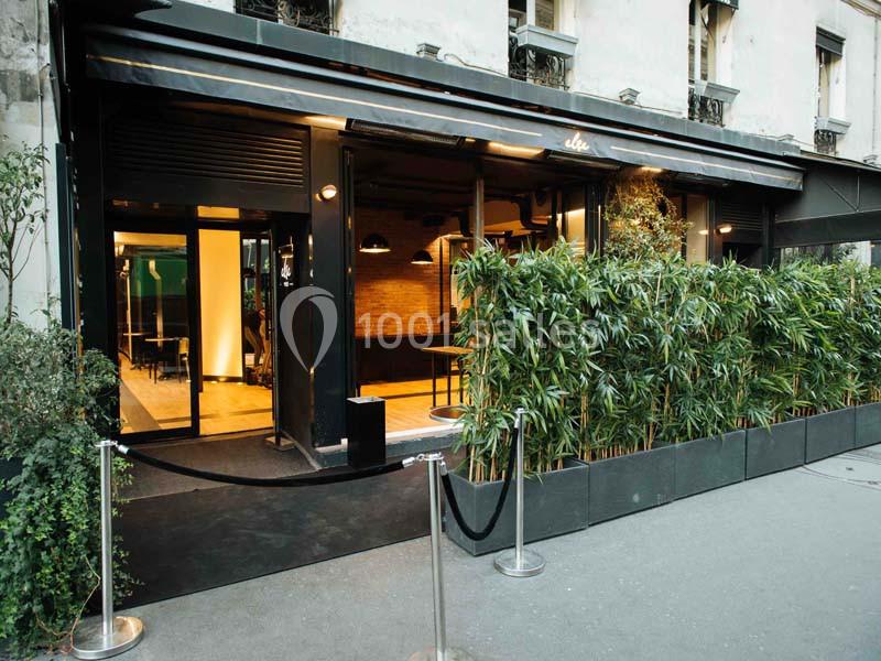 Façade d'un restaurant moderne avec une terrasse bordée de plantes et une entrée vitrée.