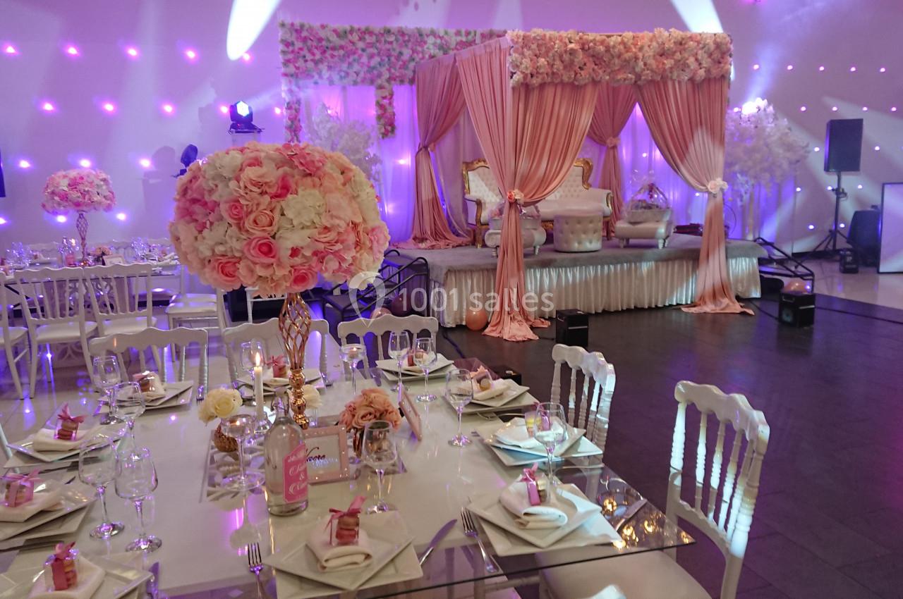 Salle de réception décorée avec des tables élégantes, des fleurs roses et blanches, et une scène ornée de rideaux et…