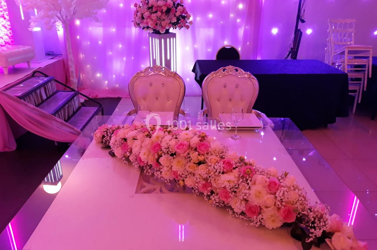 Table décorée pour un mariage avec un chemin de fleurs roses et blanches, deux chaises élégantes et un fond lumineux.
