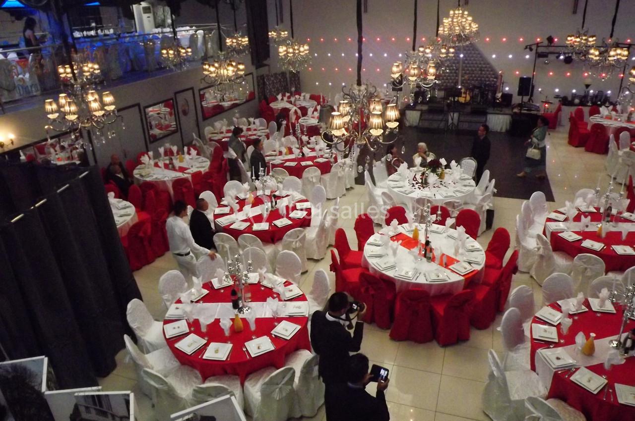 Salle de réception décorée avec des tables rondes, nappes rouges et blanches, et lustres suspendus.