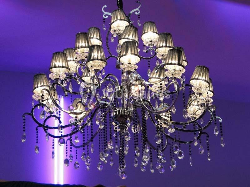 Lustre en métal noir orné de pampilles en cristal, éclairé par des abat-jours argentés dans un décor violet.