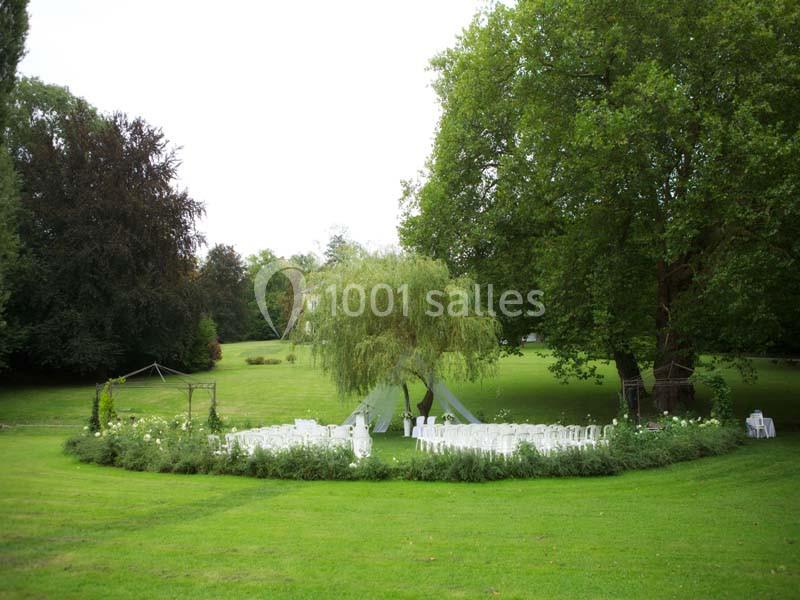 Chaises blanches disposées en cercle autour d'un saule pleureur dans un jardin verdoyant.