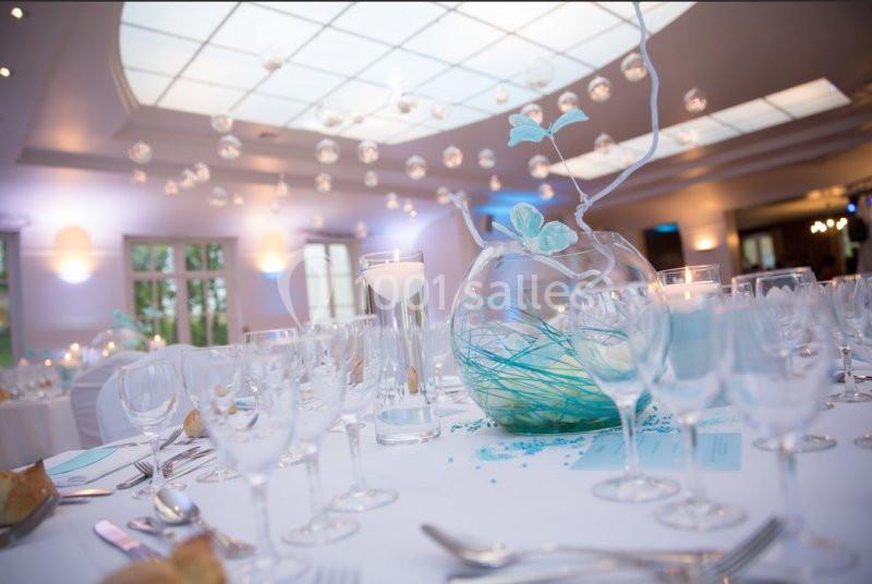 Table élégamment dressée avec des verres, des bougies et un vase décoratif dans une salle lumineuse.