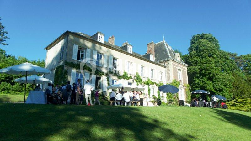 Groupe de personnes réunies devant une grande maison entourée de verdure par une journée ensoleillée.
