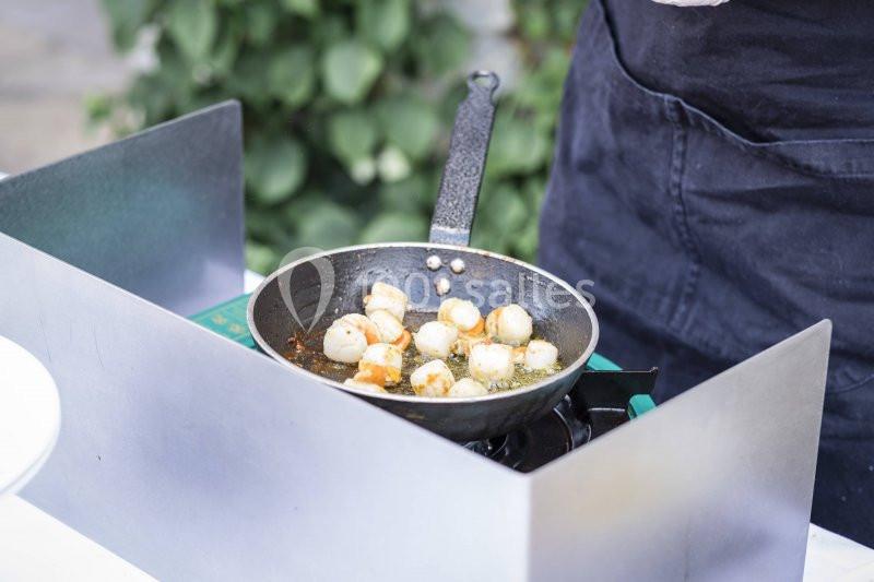 Des noix de Saint-Jacques dorées cuisent dans une poêle noire sur un réchaud en extérieur.