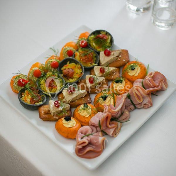 Plateau de canapés variés avec charcuterie, fromage, légumes et garnitures, présenté sur une table blanche.