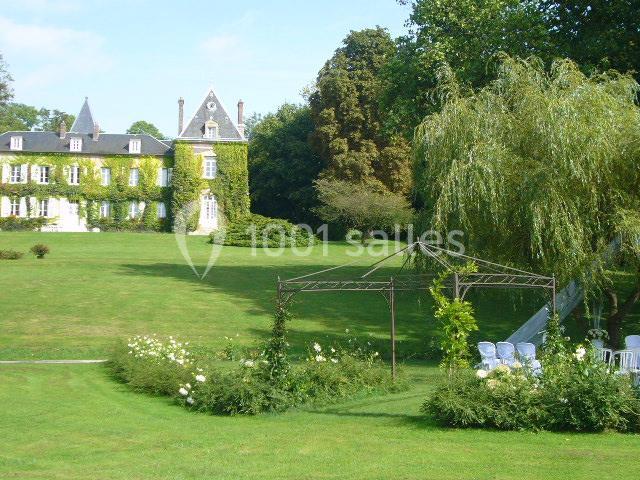 Parc verdoyant avec un château couvert de lierre en arrière-plan et une structure métallique entourée de fleurs au premier…