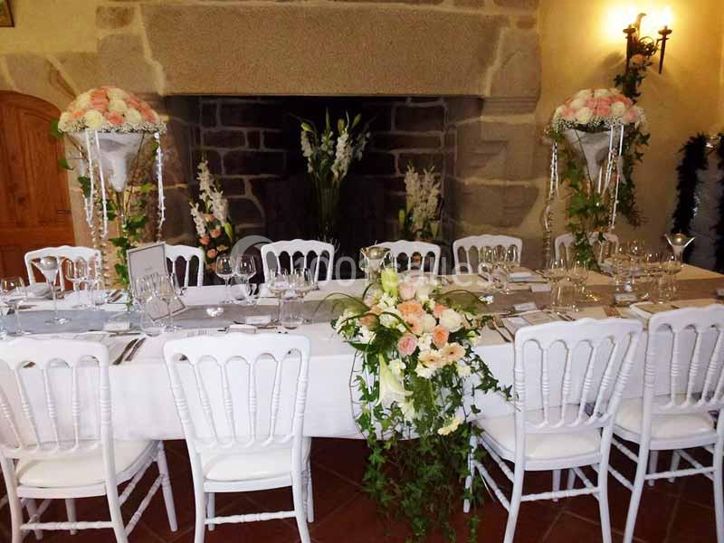 Table décorée pour un événement, avec nappes blanches, chaises assorties et compositions florales élégantes.