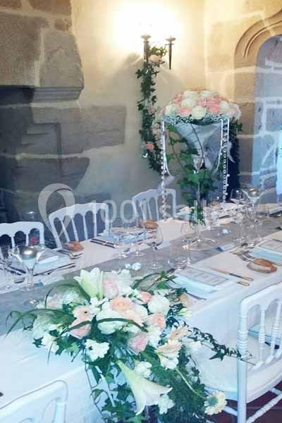 Table élégamment décorée avec des fleurs blanches et roses, nappes blanches et vaisselle raffinée dans une salle en pierre.