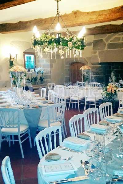 Salle de réception décorée avec des tables dressées, des chaises blanches et un lustre orné de verdure.