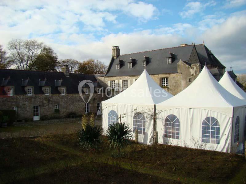 Tentes blanches installées dans la cour d'un bâtiment en pierre de style traditionnel sous un ciel partiellement nuageux.