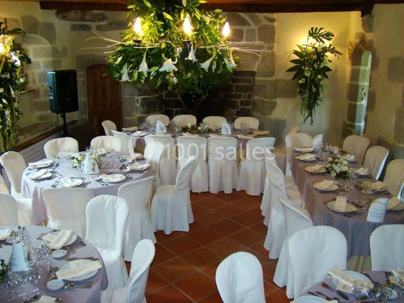 Salle décorée pour un événement avec tables rondes dressées, nappes blanches et arrangements floraux suspendus.