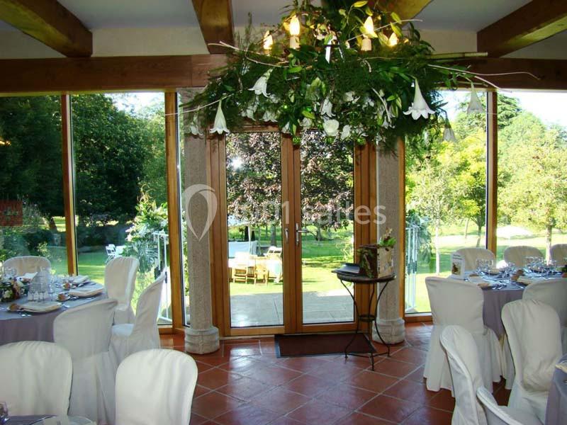 Salle de réception lumineuse avec grandes baies vitrées donnant sur un jardin verdoyant, tables dressées élégamment.