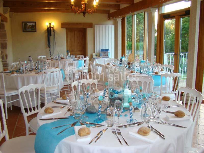 Salle de réception lumineuse avec tables rondes décorées de nappes blanches et chemins de table bleus.