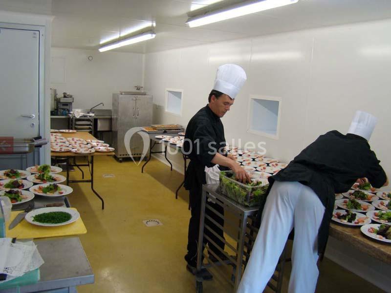 Deux chefs préparent et dressent des assiettes avec des plats colorés dans une cuisine professionnelle lumineuse.