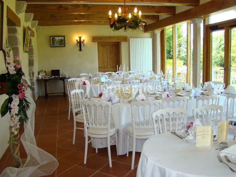 Salle de réception lumineuse avec tables rondes dressées, chaises blanches et décoration florale.