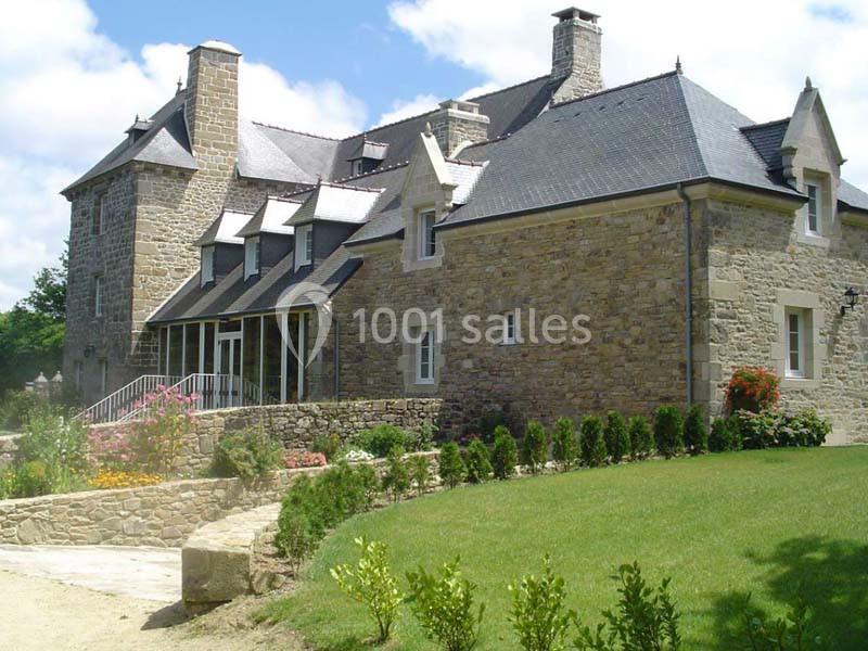 Grande maison en pierre avec toit en ardoise, entourée d'un jardin verdoyant et d'allées fleuries.