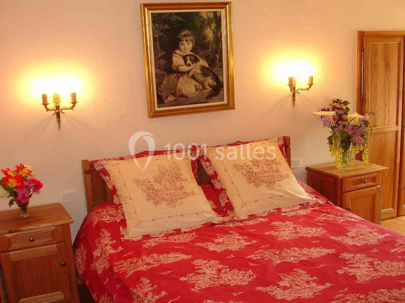 Lit double avec couvre-lit rouge à motifs, encadré par deux tables de chevet, éclairé par des appliques murales.