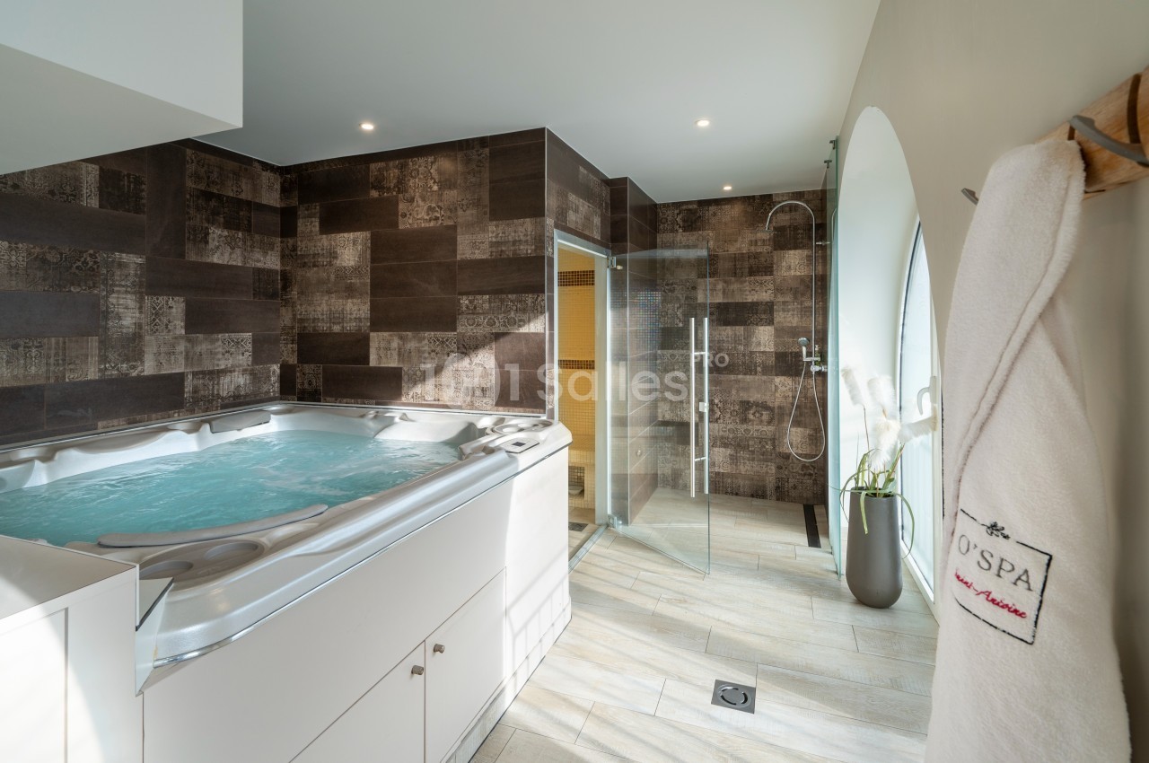 Salle de spa avec jacuzzi, douche à l'italienne, murs en carrelage foncé et peignoir suspendu.