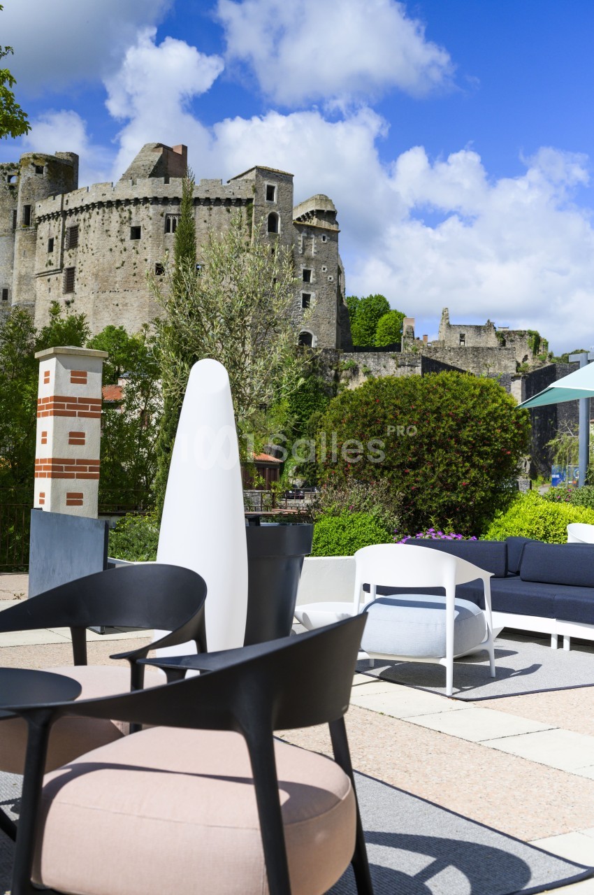Mobilier de terrasse moderne avec vue sur un château médiéval sous un ciel bleu partiellement nuageux.