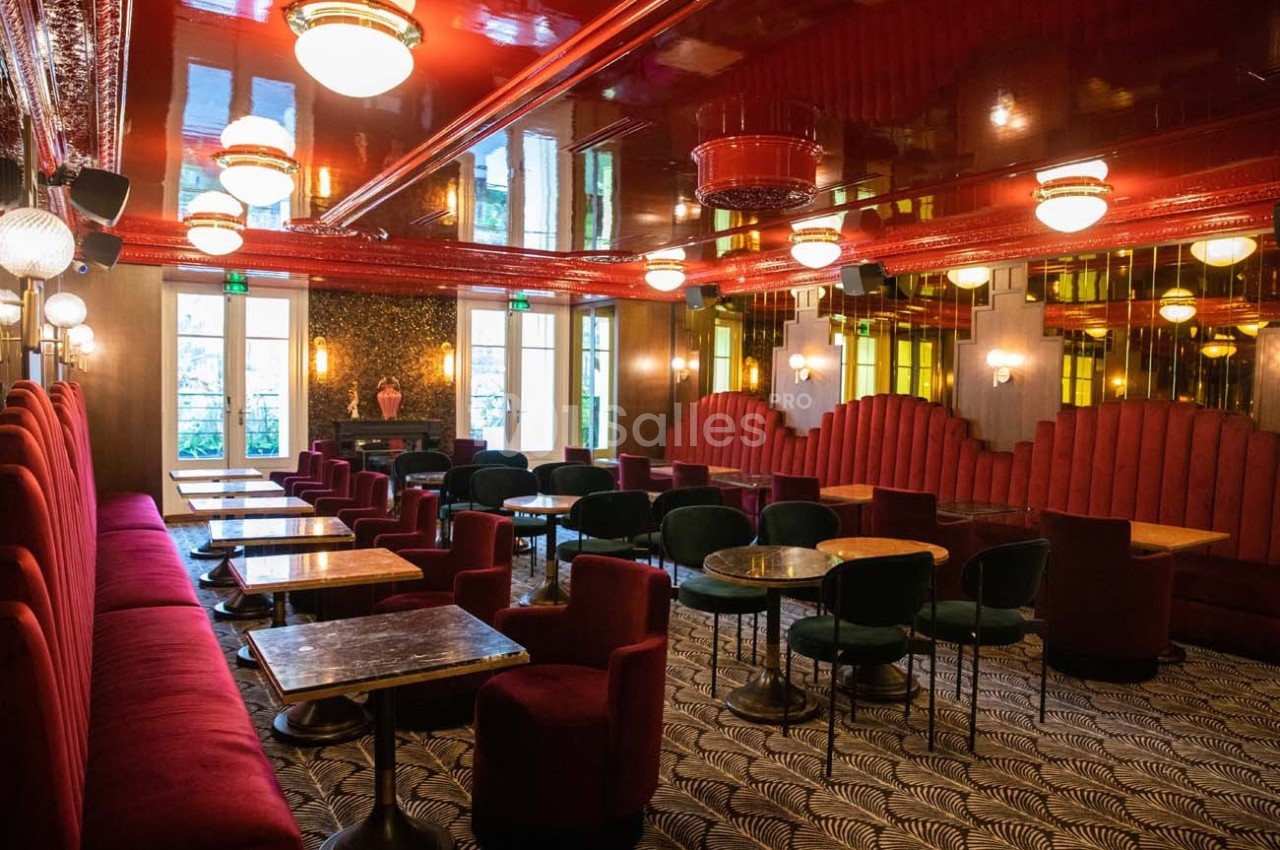 Salle élégante avec banquettes rouges, tables en marbre, chaises vertes et plafond brillant éclairé par des luminaires.