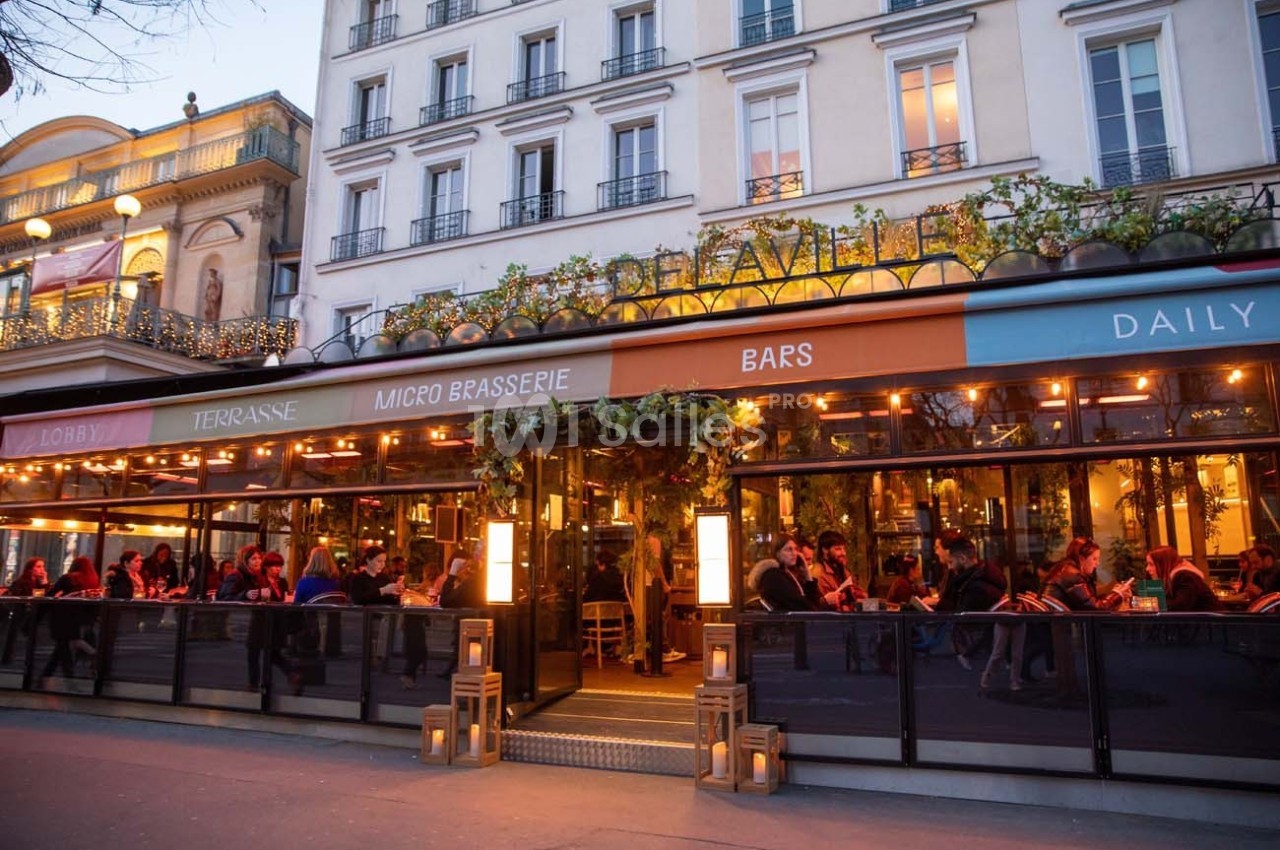 Façade d'un café-restaurant animé avec terrasse éclairée, situé au rez-de-chaussée d'un immeuble parisien.