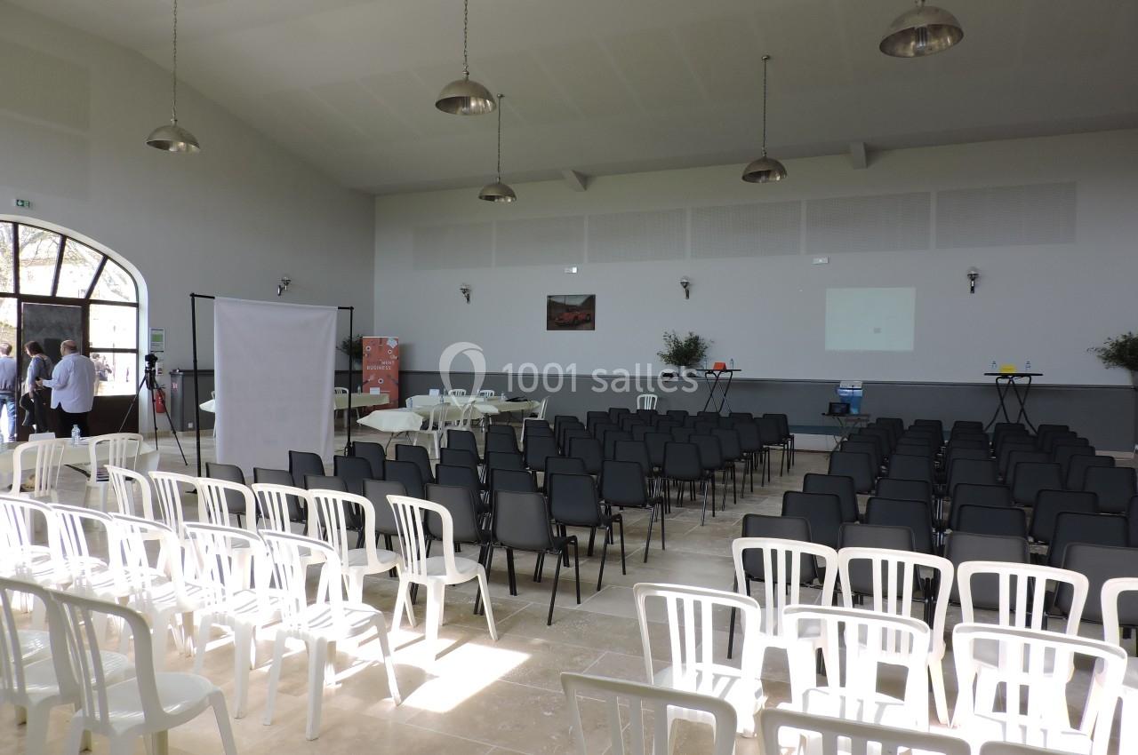 Salle de conférence lumineuse avec des rangées de chaises blanches et noires disposées face à un écran de projection.