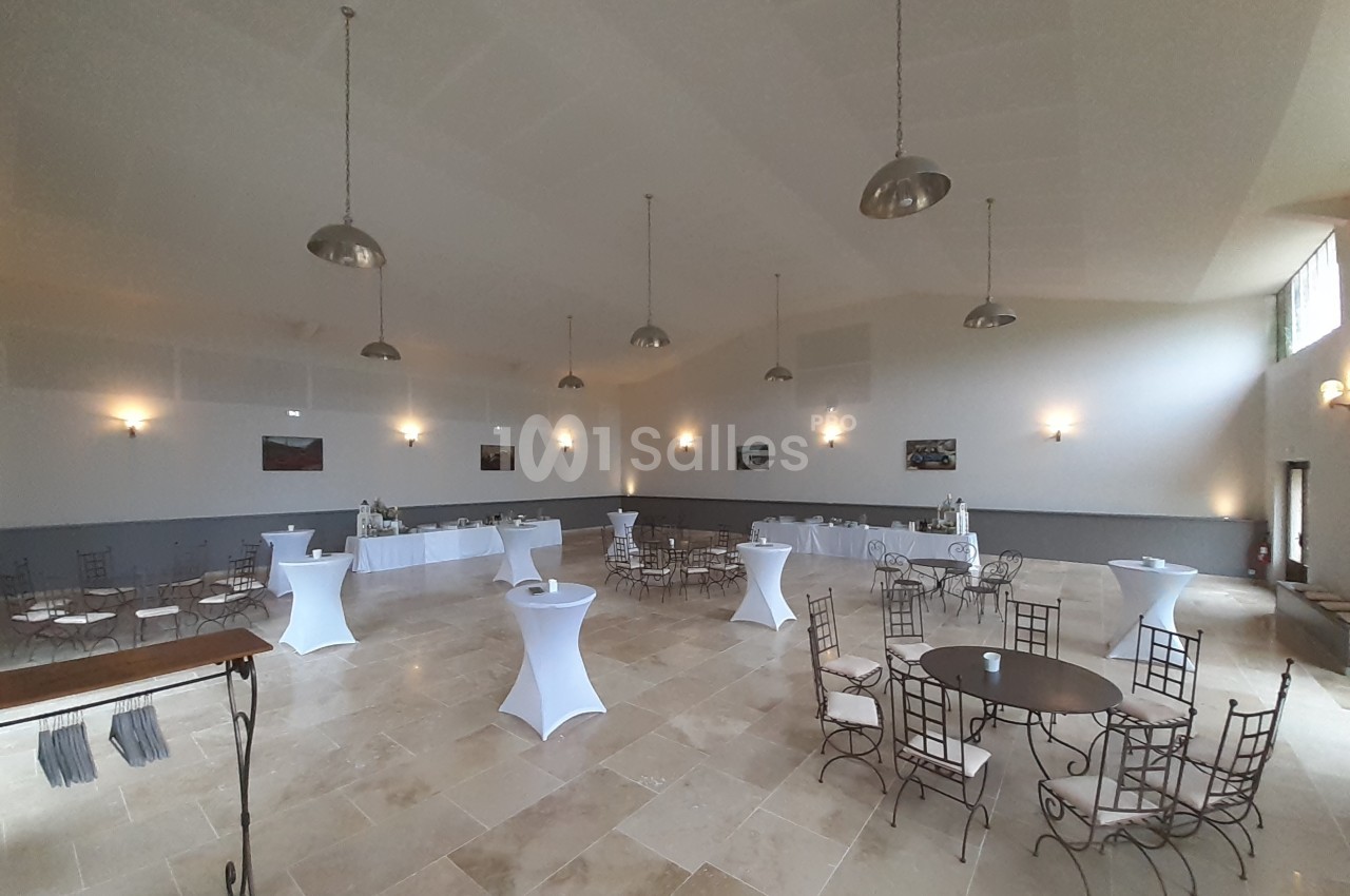 Salle de réception lumineuse avec tables rondes, chaises en métal et mange-debout, décor sobre et murs clairs.