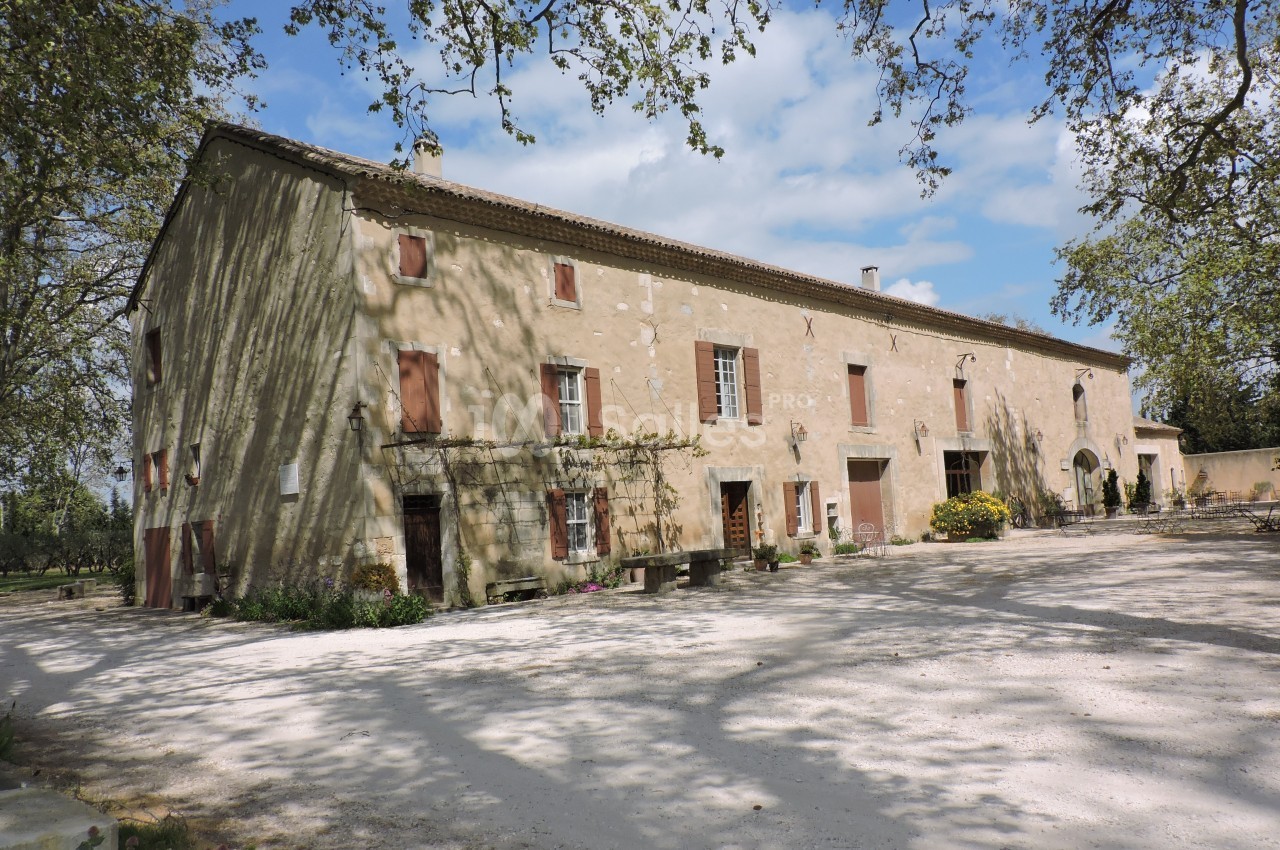 Bâtisse ancienne en pierre avec volets rouges, entourée d'arbres, sous un ciel partiellement nuageux.